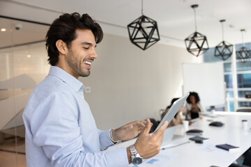 Smiling Latin businessman using modern digital tablet device standing in conference room, preparing...