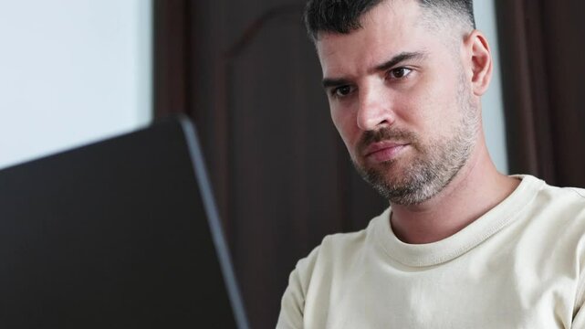 Close up portrait of black haired man looking seriously in screen of laptop. 