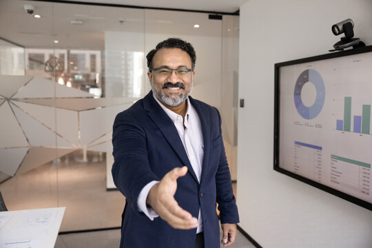Happy middle-aged 45s Indian businessman in formal suit extending his arm for handshake, greeting client, gesture of acquaintance, conclusion of deal, start partnership or collaboration with partner