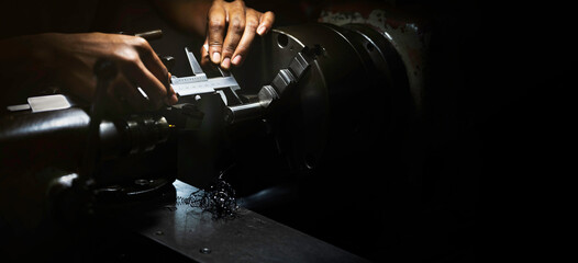 Lathe operator using a vernier caliper to measure steel workpiece dimensions at industrial workshop, showcasing precision metalworking techniques and hands-on manual engineering craft