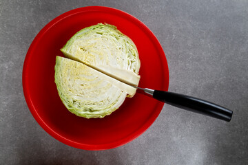 knife slicing cabbage in plastic red bowl
