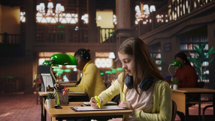 Teenager girl highlighting the important notes for the studying session, employing learning materials from the library database to complete her textbook and be productive. Academic success. Camera A.