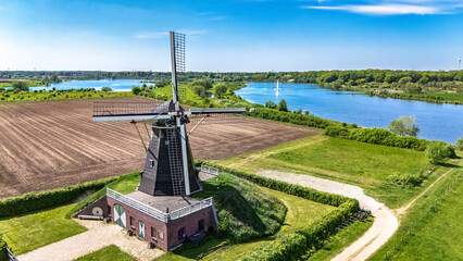 Aerial drone view of typical Dutch countryside landscape with traditional old windmill, fields and river Meuse in spring, the Netherlands