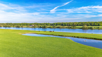 Aerial drone view of typical Dutch countryside landscape with green meadow, horses and waterfowls, peaceful rural landscape with river Meuse in spring, the Netherlands