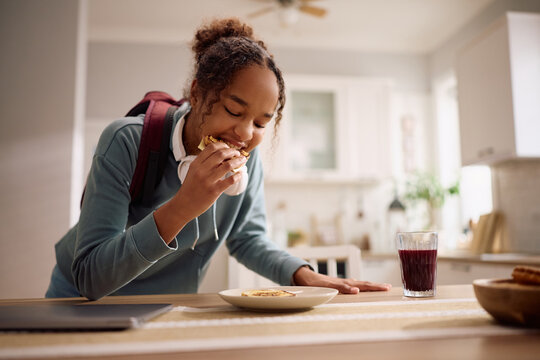 Black female student eating breakfast before going to school.