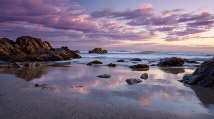 Naklejka premium Reflections of a purple-hued sky grace the wet beach, surrounding dark stones that sit peacefully in the tranquil water. Serene scene. .