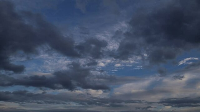 Timelapse shot of cloudy sky, flowing, billowing, moving horizontally, from right to left, blue clouds during sunset in dark color tone. Changeable weather