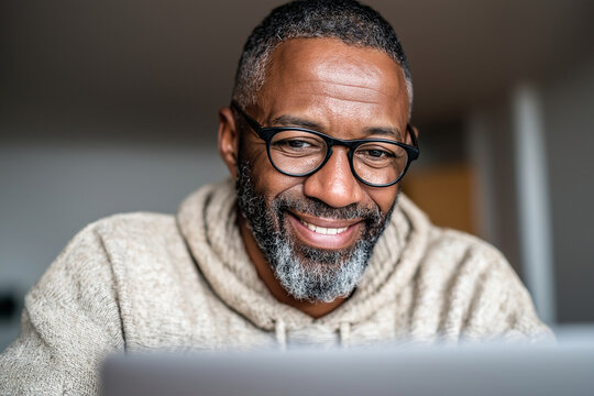  Photo of a middle-aged Hispanic man on a video call during onboarding for a remote IT job, smiling nervously at the screen. Over the shoulder shot from laptop view. Digital ligh