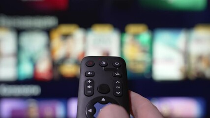 Hand Holding a Remote Control Browses Various Streaming Services On a Large Screen in a Comfortable Living Room Setting. Person Browsing Streaming Services Using Remote Control.