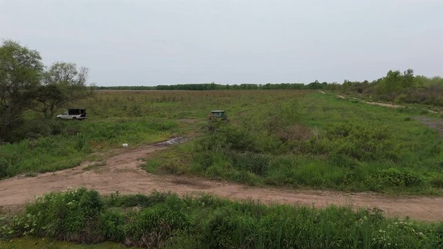 Aerial drone clip going over tractor with subsoiler working on agriculture fields in the afternoon, with deeply cloudy day and distant horizon.