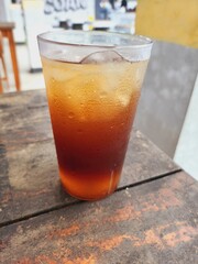 Iced tea drink in a clear plastic glass on a wooden table.