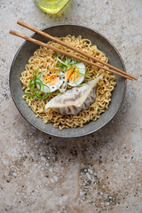 Plate of ramen noodles with boiled egg and steamed dumpling, vertical shot on a beige granite background with space, flat lay