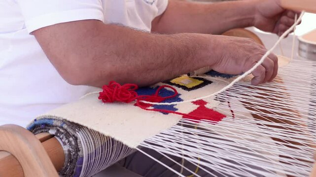 Skilled hands weave a bright geometric tapestry on a horizontal handloom, passing traditional wool yarn through taut warp threads to create an authentic handcrafted textil