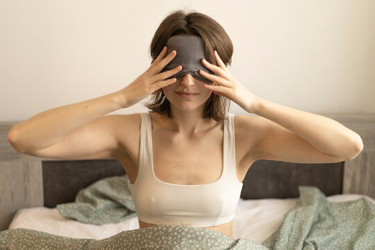 young woman wearing a sleep mask on bed holding hands near her eyes