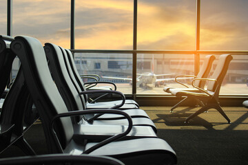 Empty chairs and passenger in the airport terminal on evening sunset light