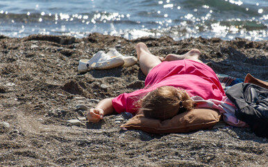 A woman is laying on the beach in a pink dress