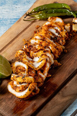 Grilled calamari cut into rings with garnishes on a wooden cutting board