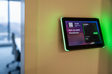 Wall-mounted tablet displaying meeting room information in an office