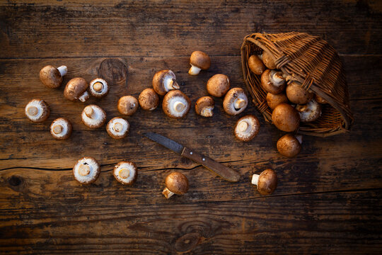 Brown mushrooms and a knife on a rustic wooden table with a willow basket