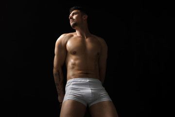 Fototapeta premium Young man in stylish white underwear on chair against black background, low angle view