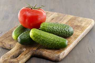 Fresh cucumbers and tomato lying on wooden cutting board