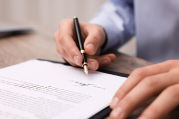 Man putting signature on document at table, closeup