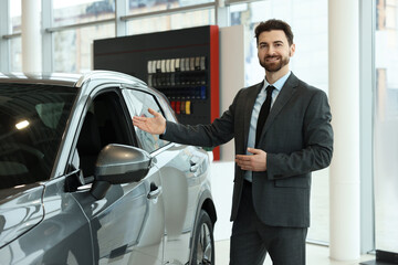 Happy salesman near new grey car in salon