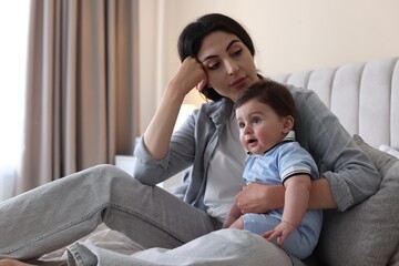 Woman suffering from postpartum depression with her little baby on bed at home. Space for text