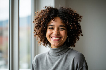 Fototapeta premium Woman with curly hair smiling at camera in front of a window, with a wall in background.