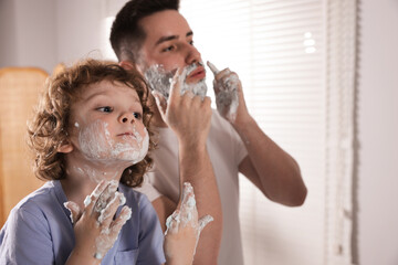 Happy father and his son with shaving cream on their faces in bathroom, selective focus