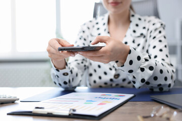 Woman taking photo of document using scanning app on smartphone at desk in office, closeup