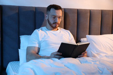 Young man reading book in bed at home