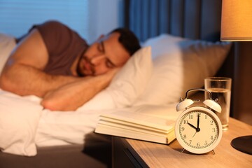 Young man sleeping in bed at home, focus on alarm clock and book