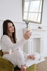 A happy young woman smiles brightly while looking at her smartphone screen, clearly engaged with entertaining content. Shot in natural indoor lighting, this authentic moment represents modern digital 