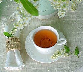 Cup of tea on the table with spring fresh bouquet with white blooming fragrant branches of bird...