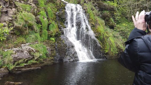 Professional photographer capturing stunning waterfall cascading through lush green irish countryside, documenting natural landscape during scenic outdoor journey