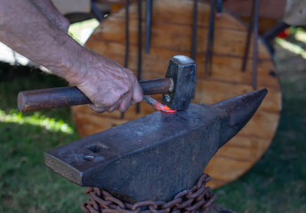 Close-up of a blacksmith's hand holding metal rod on anvil with hammer during traditional forging...