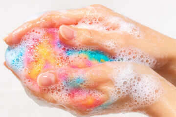 Fototapeta premium Close-up of colorful rainbow soap lathered in foamy hands. Playful, joyful and bright skincare concept.