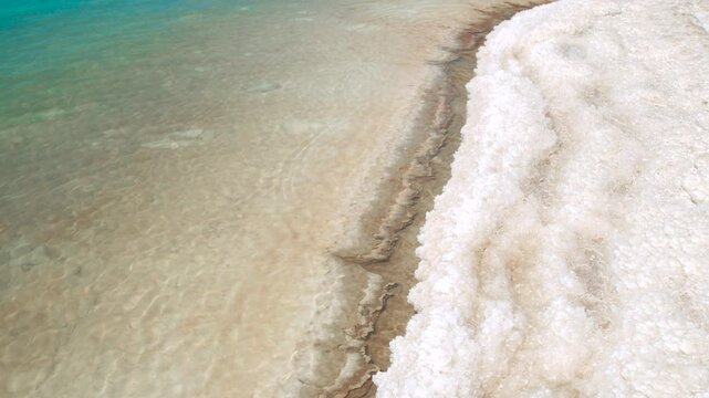 Close-up view of natural salt formations and white crystals along the edge of the Dead Sea in Jordan.