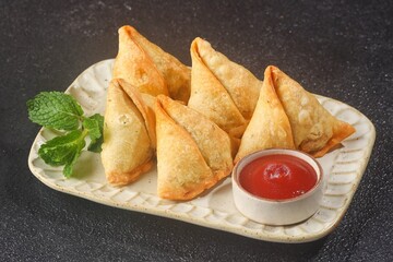 Samosa or samboosa is a triangular fried pastry filled with boiled potatoes seasoned with spices mixed with peas, onions, coriander leaves, and sometimes paneer.
