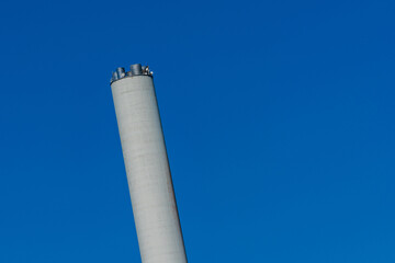 Tall industrial smokestack with satellite dishes against blue sky.
