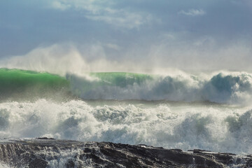 A huge green wave crashes as it breaks and wind spray flies from the top as the wave chases the one ahead on its way towards the rocks at Snapper Rocks on the Gold Coast in Queensland, Australia.
