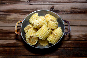Cooked corn on the cob in an aluminum pot on a rustic board