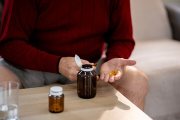 An elderly man is sitting and taking medicine in his home.