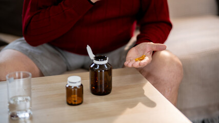 An elderly man is sitting and taking medicine in his home.