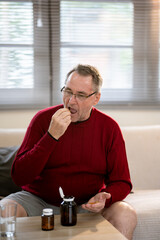 An elderly man is sitting and taking medicine in his home.