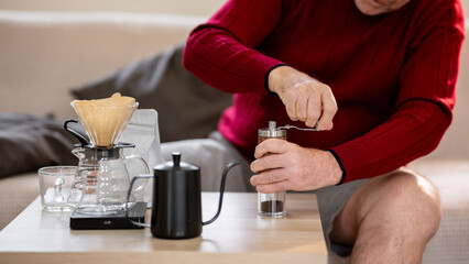 An elderly man is happily making coffee on a bright morning at his home.