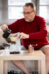 An elderly man is happily making coffee on a bright morning at his home.