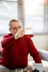 An elderly man is happily making coffee on a bright morning at his home.