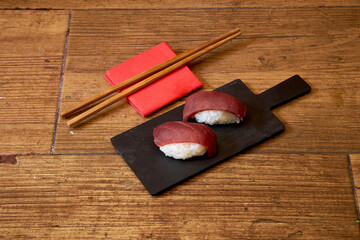A plate of sushi with chopsticks and napkins on a wooden table. The sushi is cut into two pieces